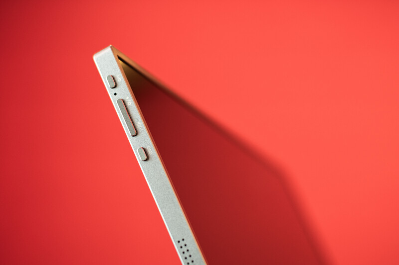 White smartphone with visible button details casting a distinct shadow on a coral red background.