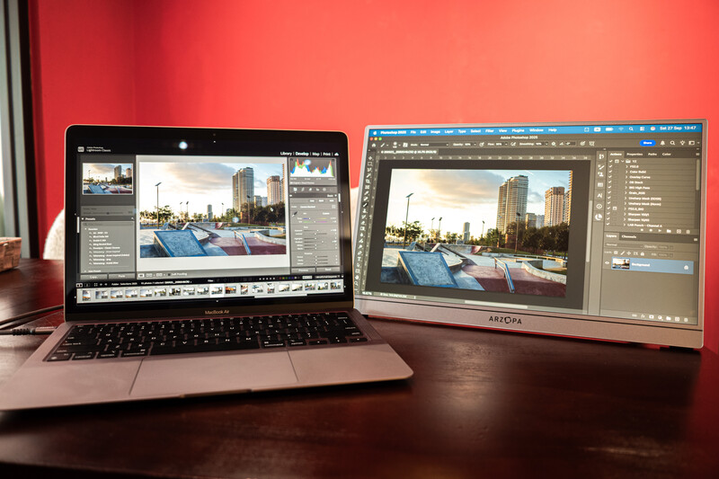 Laptop and external monitor displaying photo editing software with an urban architectural image open on both screens.