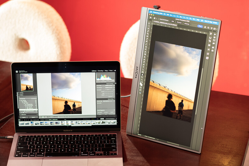 Laptop and external monitor displaying photo editing software with sunset silhouette image open side-by-side.