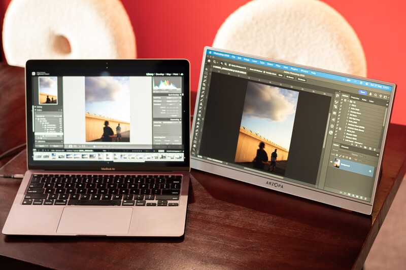 Two laptops displaying photo editing software with a silhouetted landscape image open on both screens.