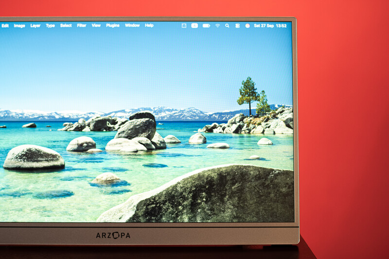 Alpine lake with turquoise water, granite boulders, and snow-capped mountains displayed on an ARZOPA monitor against a red background.