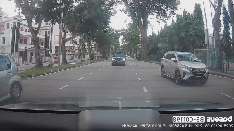 Dashboard camera view of a tree-lined urban street with multiple vehicles and colonial-style buildings.