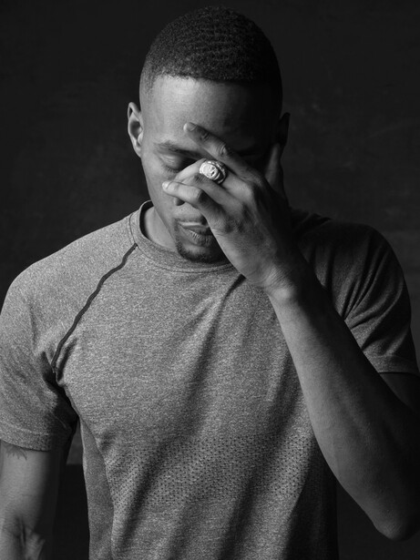 Man in gray t-shirt with hand to face against dark background.