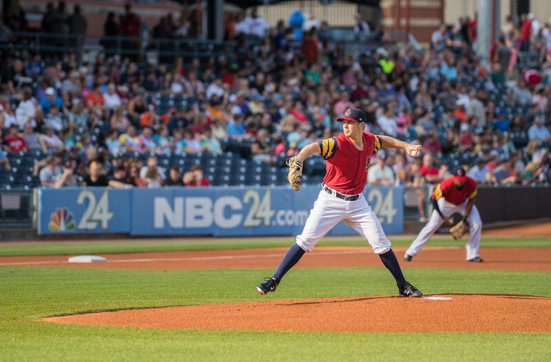 Baseball pitcher in red uniform mid-delivery on the mound during a stadium game.