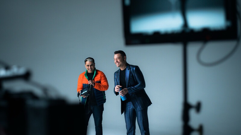 Two professionals walking and conversing in a studio with dramatic lighting and blue-tinted backdrop.