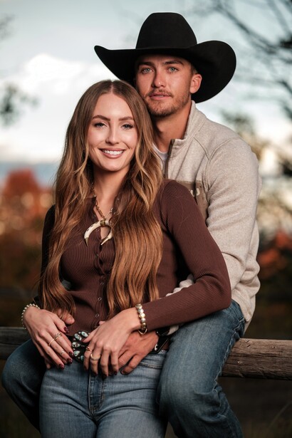 Couple posing together outdoors, man wearing cowboy hat and brown shirt, woman in brown top and jeans.