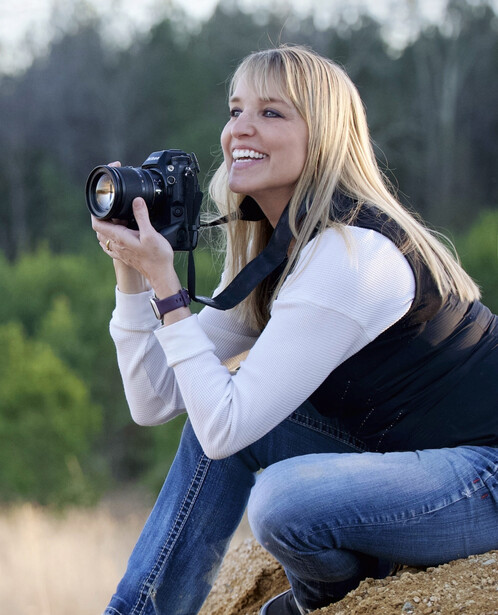 Female photographer holding a professional video camera while crouching outdoors.