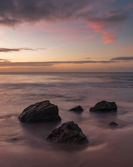 Rocky outcrops emerging from misty ocean waters during golden hour sunset.