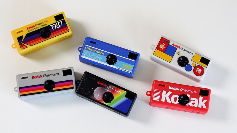 Six colorful Kodak Camara single-use film cameras arranged on a white surface.