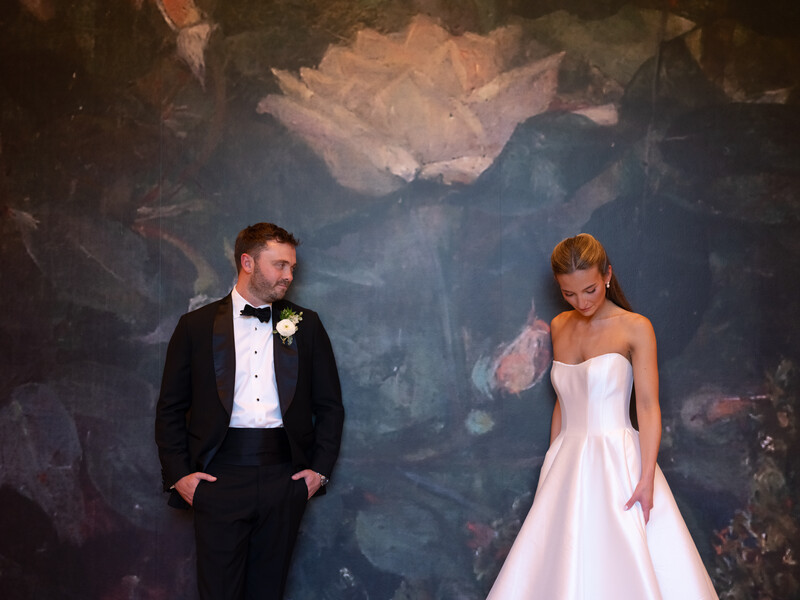 Bride and groom standing apart against an artistic painted backdrop during formal portrait session.