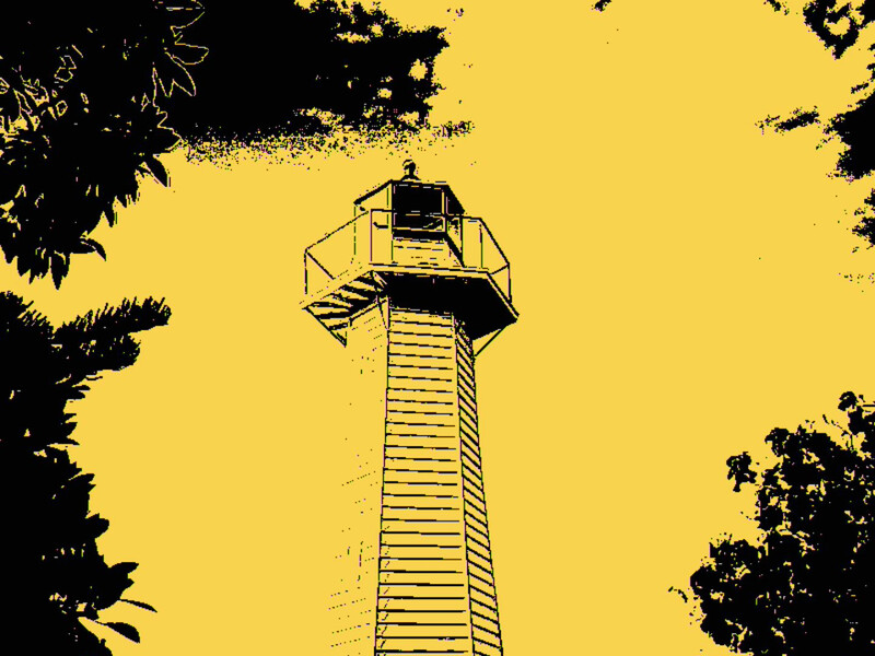 Lighthouse tower with metal railing against bright yellow sky, framed by dark foliage.