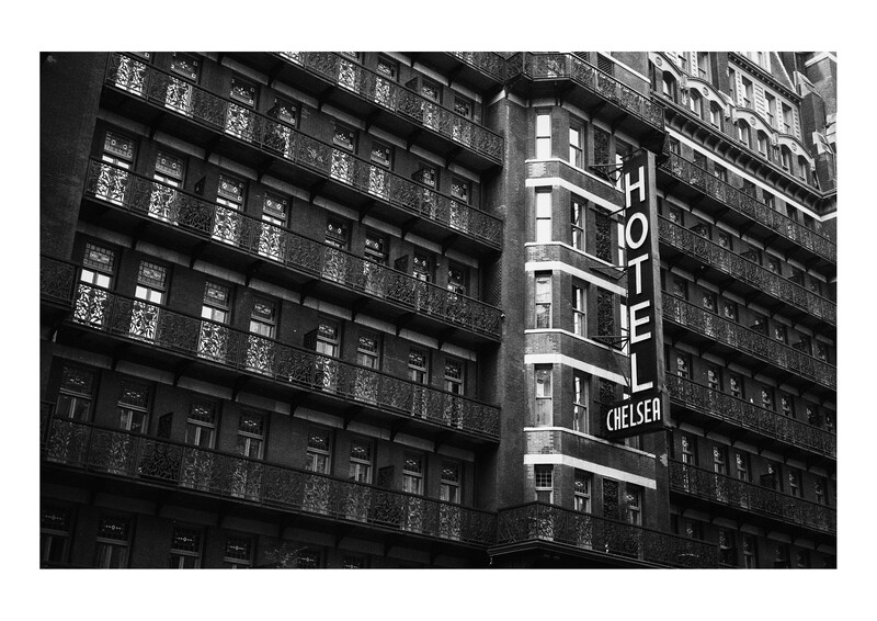 Vertical neon hotel sign on a mid-century building facade in black and white photography.