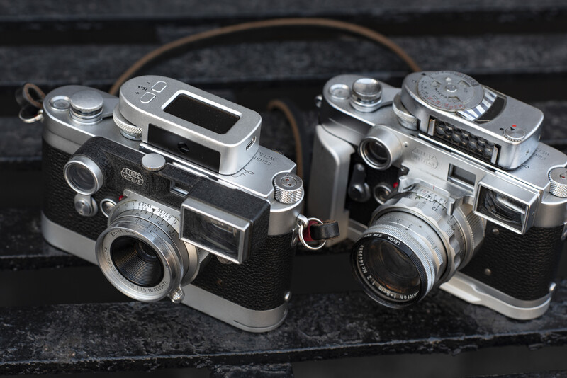 Four vintage rangefinder cameras with chrome and black bodies arranged on a dark slate surface.