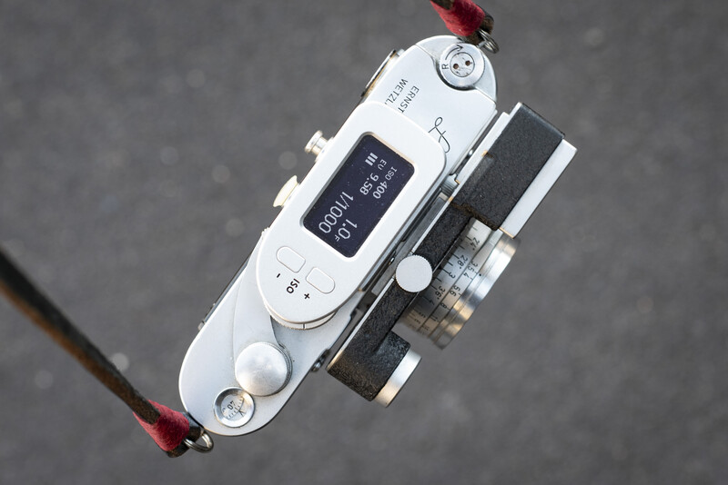 Top-down view of a vintage rangefinder camera with white body and black lens attached to gray background.