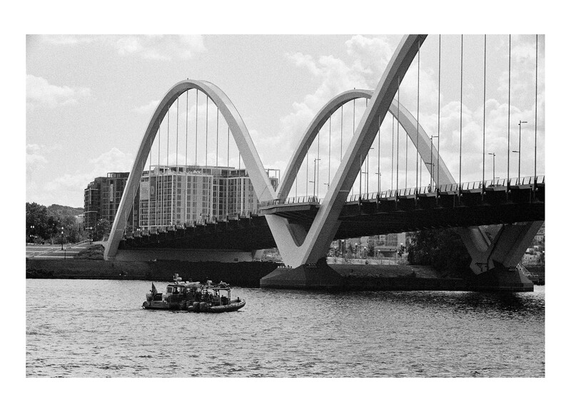 Undulating cable-stayed bridge with twin arches spanning a river, a small passenger ferry passing beneath.