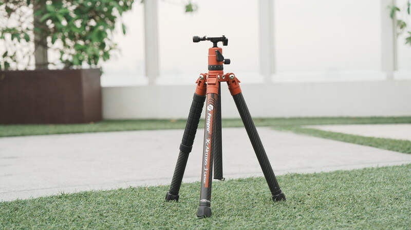 Orange and black tripod with ball head mounted on artificial turf indoors.