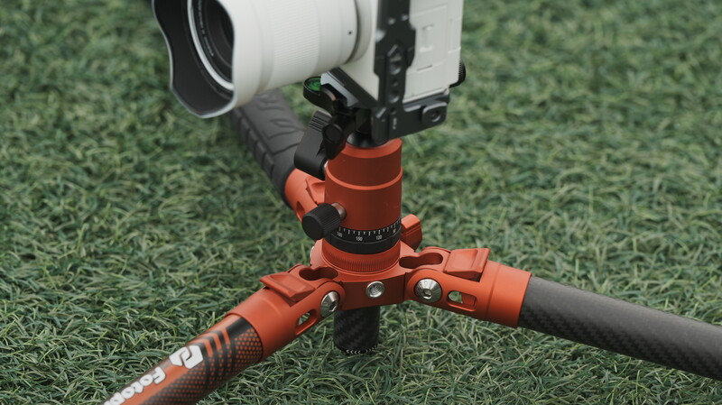 Orange ball head with pan-tilt mechanism mounted on tripod with white camera rig above on grass.