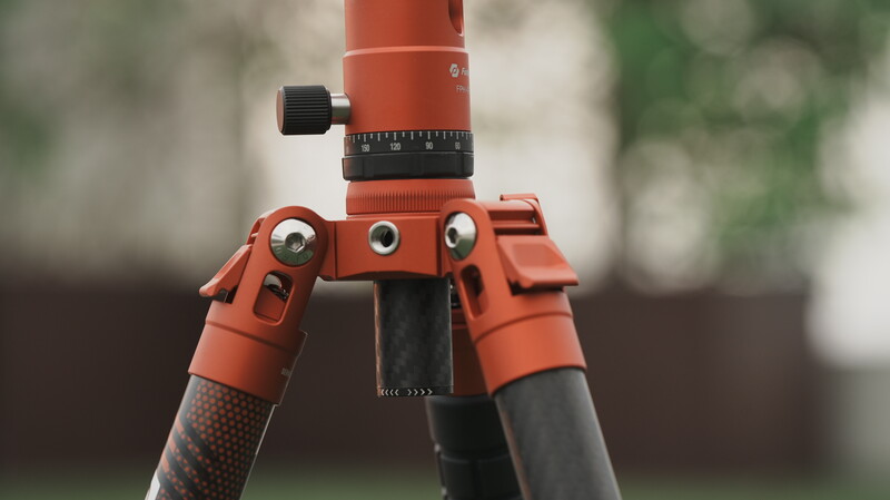 Close-up of a red surveying tripod head with adjustment knobs and graduated measurement scale.