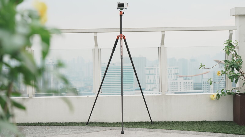 Camera tripod with smartphone mount on rooftop garden overlooking urban cityscape.