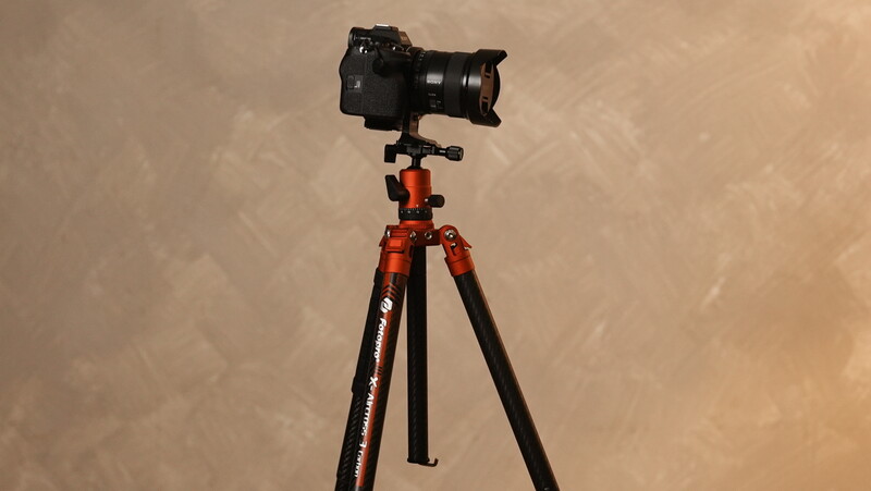 DSLR camera mounted on red tripod with ball head against textured beige wall.