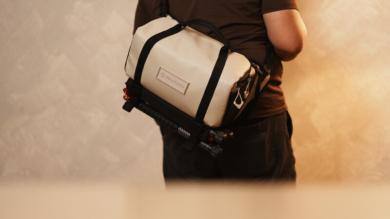 Person wearing a black shirt with a cream and black messenger bag across their chest.