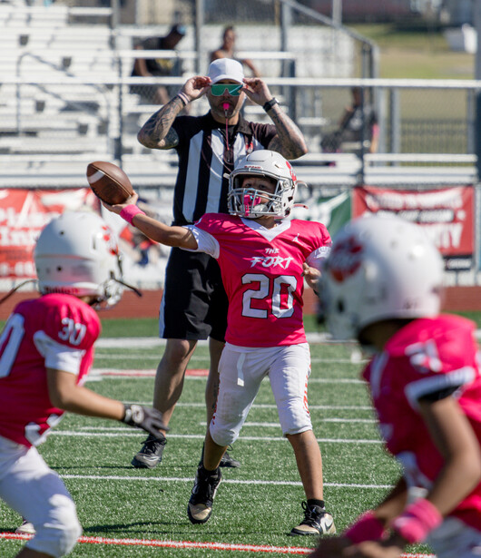 Youth football player jumping to catch a pass during practice, with teammates visible in the background.