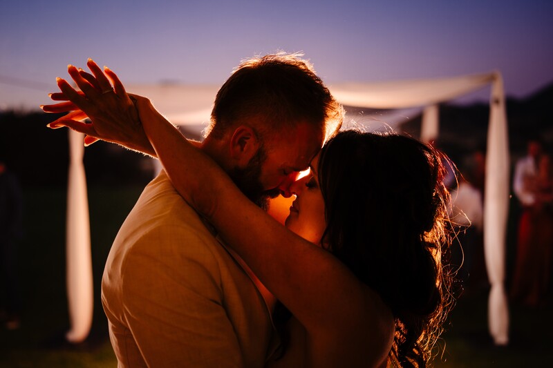 Couple embracing at sunset with backlighting creating a warm glow around their silhouettes.
