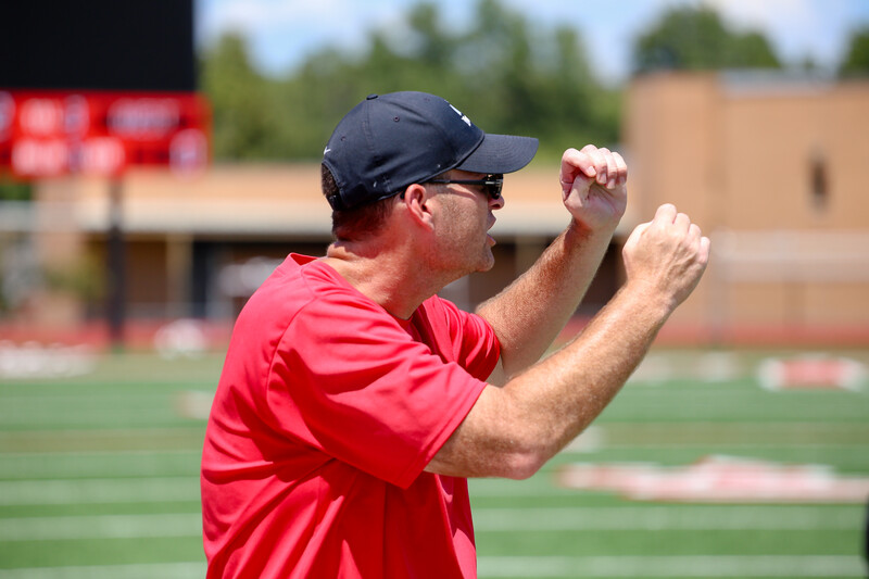 Baseball coach demonstrating throwing technique with baseball in hand on field.