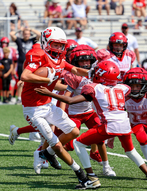 Youth football player in red uniform evading defenders during a game on grass field.