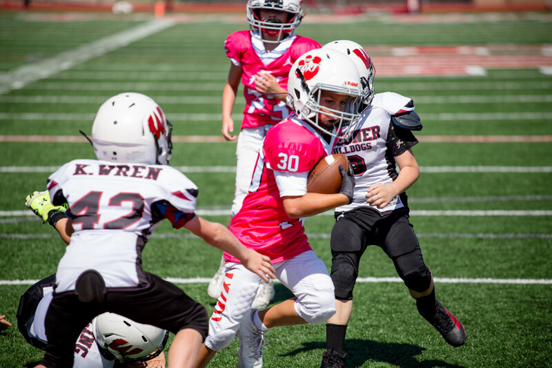 Youth football player in pink jersey evading defenders during a game on an outdoor field.