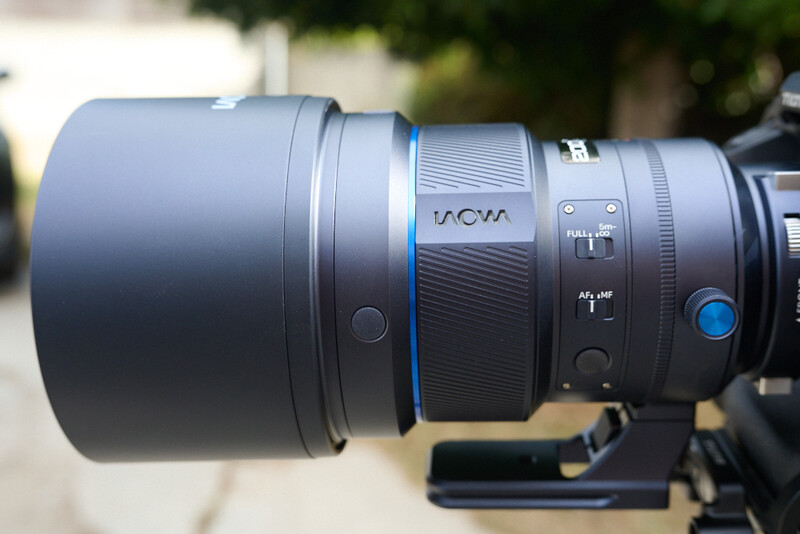 Macro view of a telephoto lens barrel showing focus ring, aperture controls, and blue accent ring details.