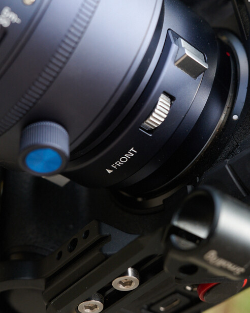 Close-up of a cinema lens with focus ring and L-mount designation on professional camera rig.