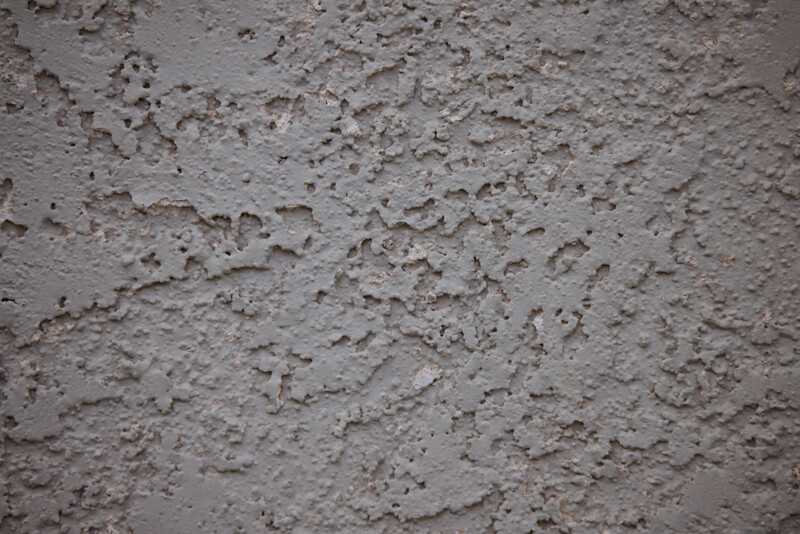 Close-up of textured concrete or stucco surface with rough, uneven finish and visible aggregate particles.