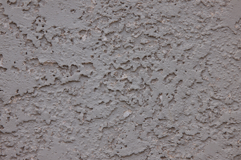 Close-up of textured concrete or plaster surface with rough, uneven finish and scattered aggregate particles.