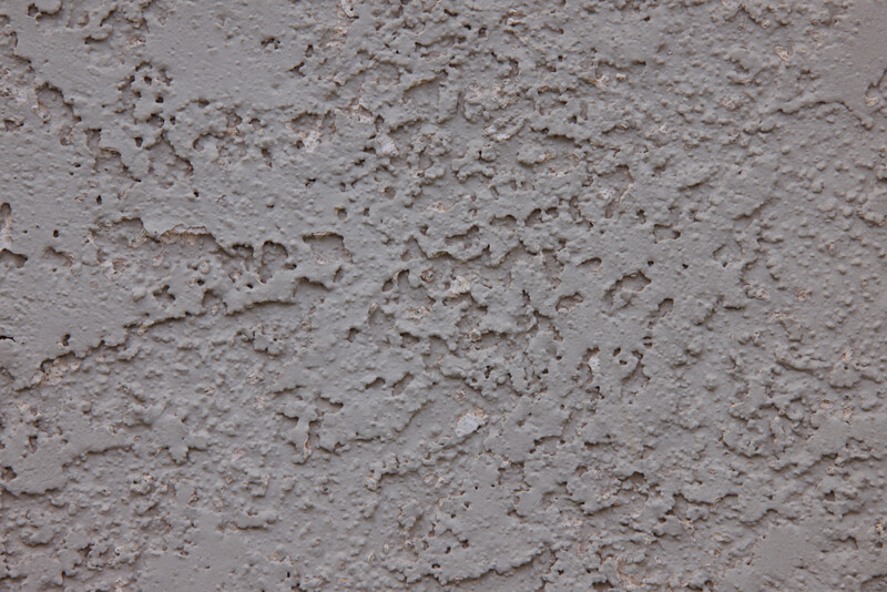 Close-up of rough concrete or stucco wall surface with uneven texture and shadows.