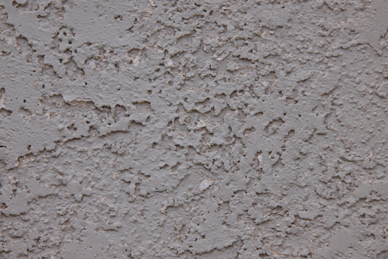 Close-up of textured concrete wall surface with rough, uneven finish and scattered aggregate particles.