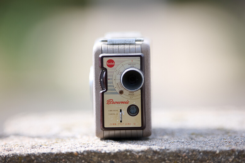 Vintage Brownie movie camera with cream-colored body and red branding, positioned on a textured surface.