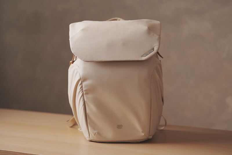 Cream-colored backpack with padded flap and side handles displayed on wooden surface.