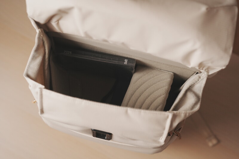 Open cream-colored camera bag revealing black camera body and beige quilted pouch inside.