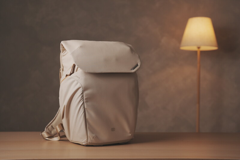 Minimalist still life with cream-colored backpack and wooden floor lamp against textured brown wall.