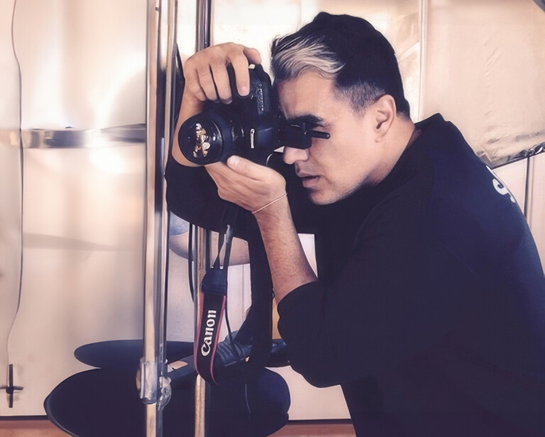 Photographer holding a DSLR camera up to his eye while composing a shot in an indoor studio setting.