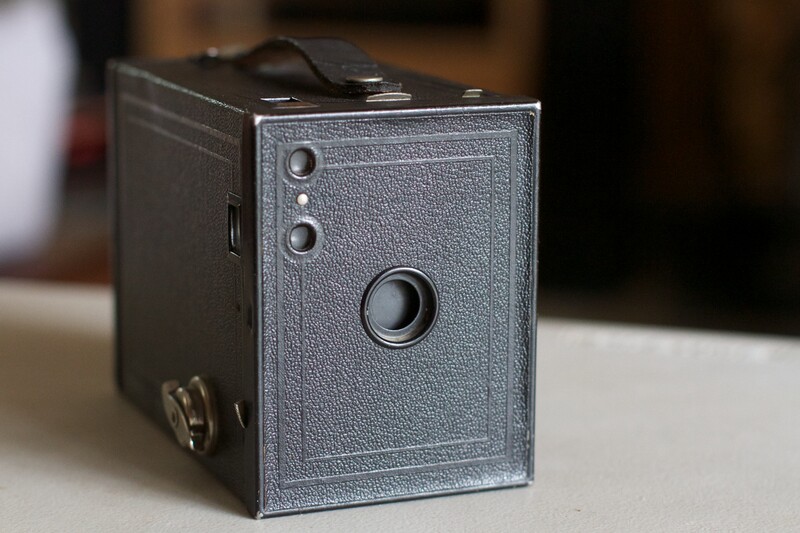 Vintage box camera with textured gray body and single large lens element.
