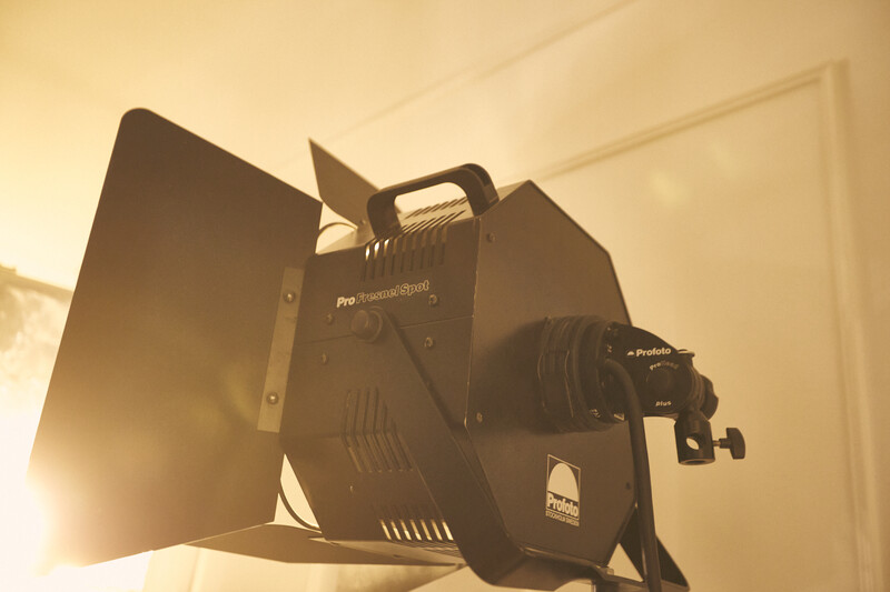 Professional LED film light with barn doors and lens attachment mounted on stand.