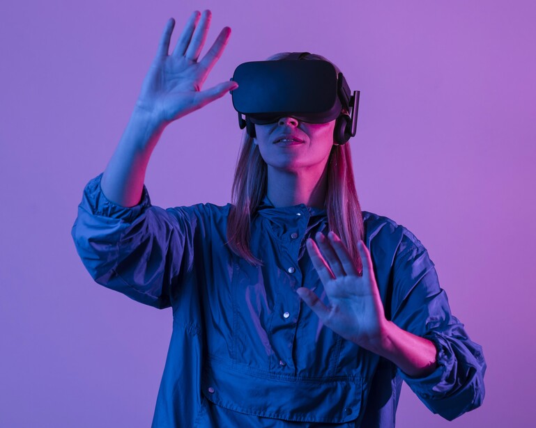 Person wearing VR headset with hand raised against purple and blue neon lighting.