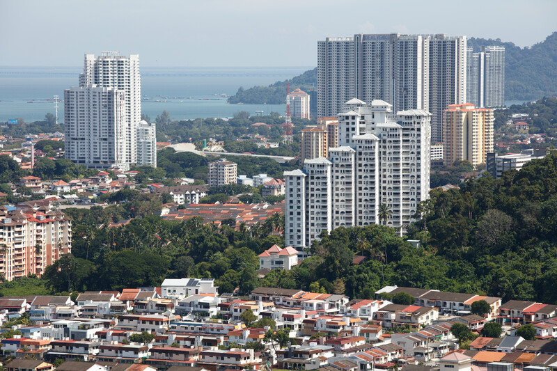 Elevated view of a tropical hillside city with high-rise residential towers overlooking residential neighborhoods and distant water.