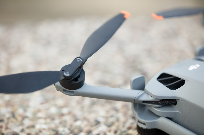 Close-up of a gray quadcopter drone with extended propeller arms on a sandy surface.