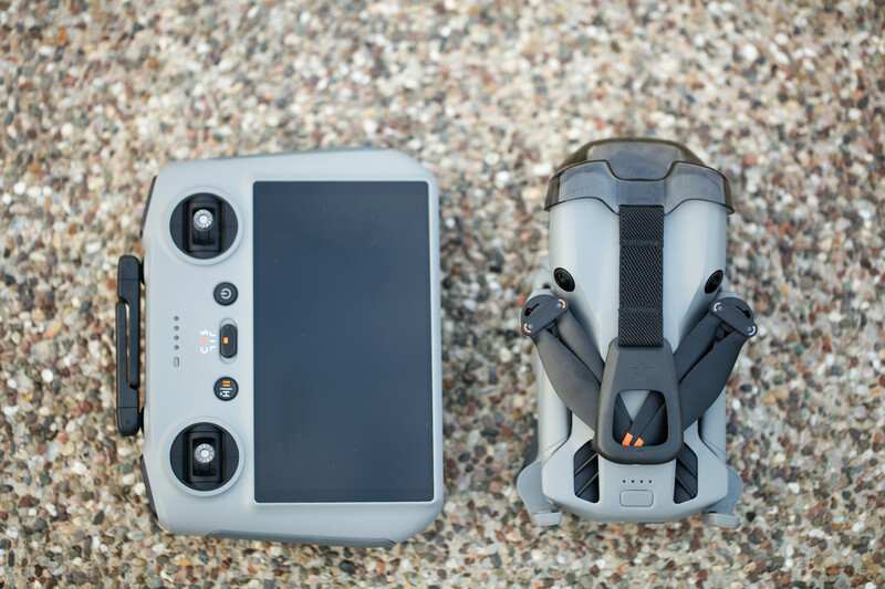 Overhead flat lay of a drone remote controller and aircraft body on a textured sand surface.