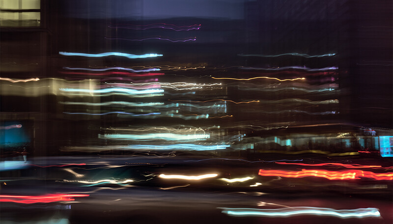 Long exposure photograph of vehicle headlights and taillights streaking horizontally across a dark urban scene.