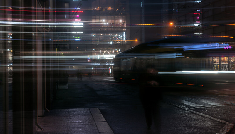 Night street scene with motion-blurred vehicle and illuminated building windows creating layered light trails.