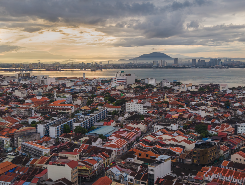 Aerial cityscape with terracotta roofed buildings, waterway, and distant mountain at golden hour.